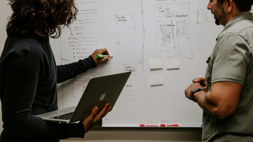 Two colleagues mapping out a website plan on a whiteboard