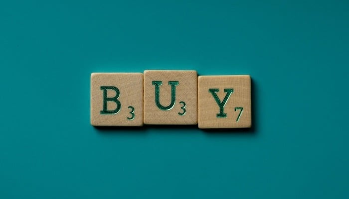 three scrabble pieces spelling the word buy on a green background